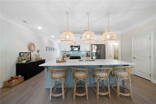 kitchen featuring decorative light fixtures, a center island with sink, appliances with stainless steel finishes, sink, and white cabinetry