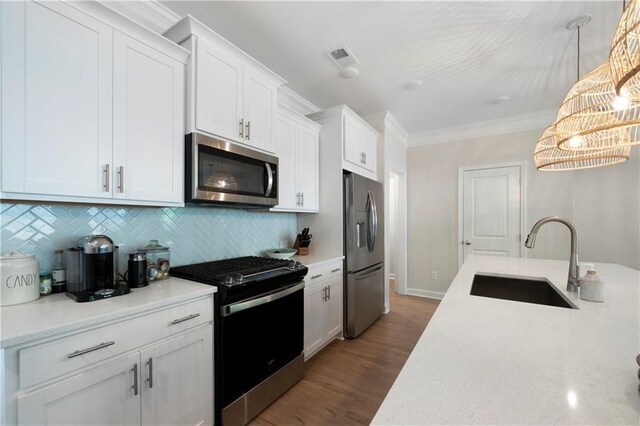 kitchen with white cabinets, hardwood / wood-style floors, appliances with stainless steel finishes, sink, and pendant lighting