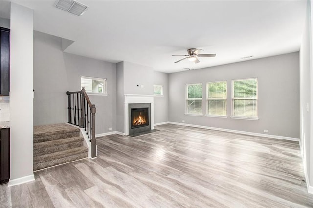 unfurnished living room with a ceiling fan, stairway, baseboards, and light wood-style floors