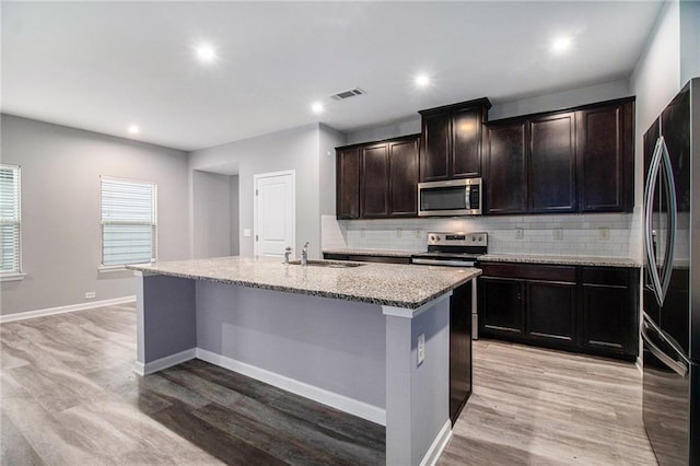 kitchen featuring stainless steel appliances, a sink, light wood-type flooring, decorative backsplash, and recessed lighting