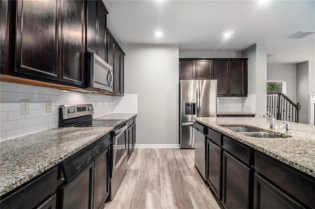 kitchen with appliances with stainless steel finishes, a sink, light stone counters, light wood finished floors, and tasteful backsplash