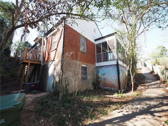 view of home's exterior featuring a deck, brick siding, stairway, and a sunroom