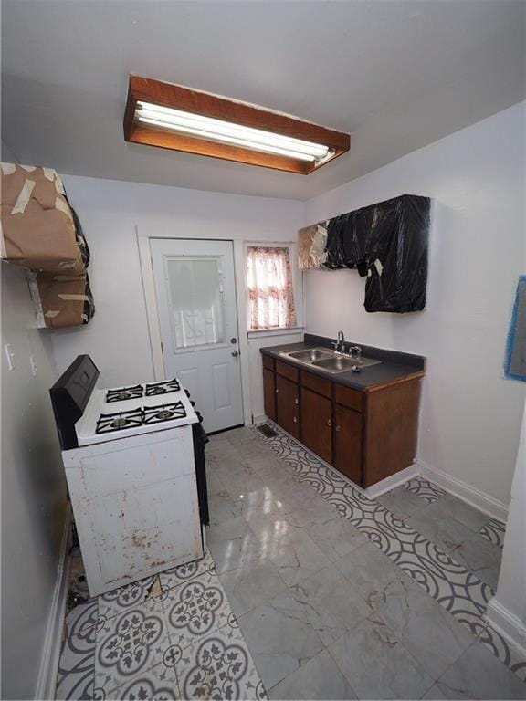 kitchen with dark countertops, marble finish floor, baseboards, and a sink