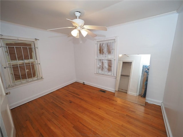 unfurnished room with ceiling fan, wood finished floors, visible vents, baseboards, and ornamental molding