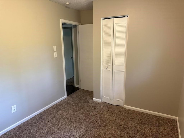 unfurnished bedroom featuring baseboards, a closet, dark carpet, and a textured ceiling