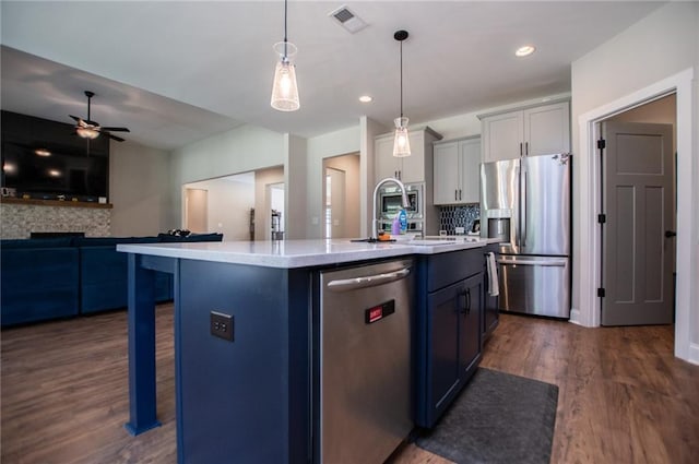 kitchen featuring a kitchen bar, hanging light fixtures, appliances with stainless steel finishes, dark hardwood / wood-style floors, and a kitchen island with sink