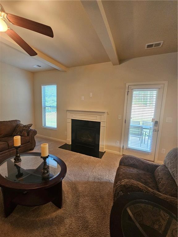 living area featuring beam ceiling, carpet flooring, a fireplace with flush hearth, ceiling fan, and baseboards