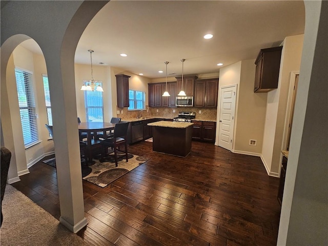 kitchen with appliances with stainless steel finishes, a kitchen island, dark wood-style flooring, dark brown cabinets, and decorative backsplash