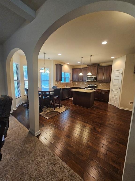 kitchen featuring appliances with stainless steel finishes, arched walkways, light countertops, open floor plan, and dark brown cabinetry