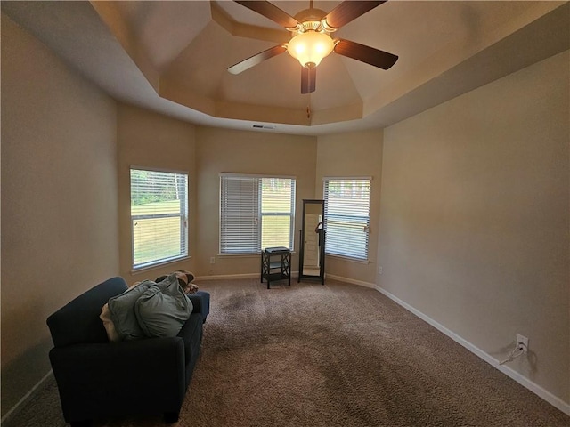 living area featuring a tray ceiling, baseboards, carpet floors, and a ceiling fan