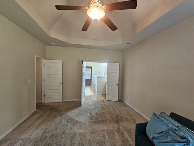 unfurnished bedroom with a tray ceiling, carpet flooring, baseboards, and a ceiling fan