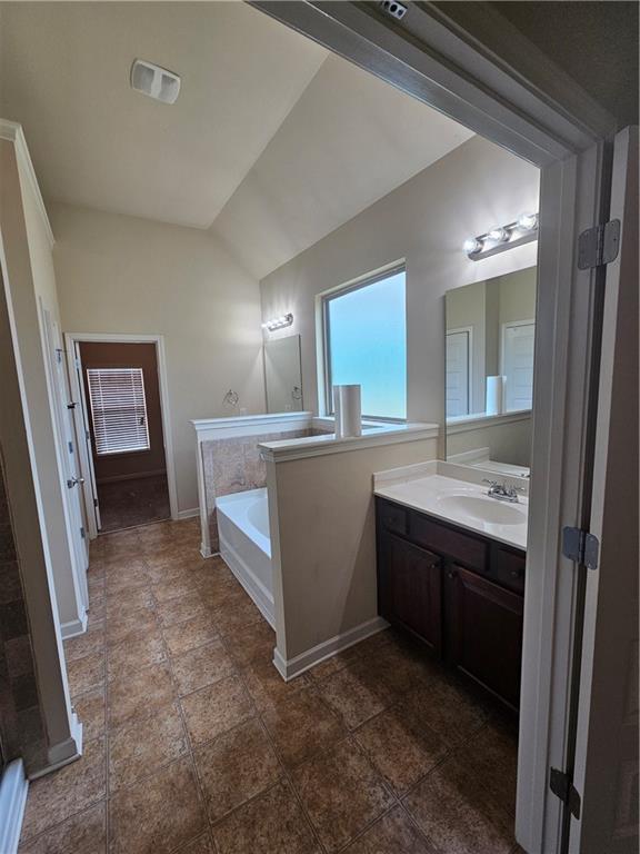 bathroom with lofted ceiling, vanity, a garden tub, and baseboards