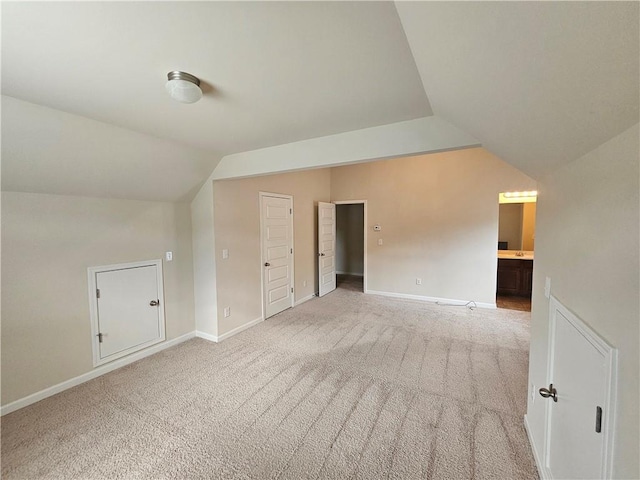 additional living space featuring vaulted ceiling, light colored carpet, and baseboards
