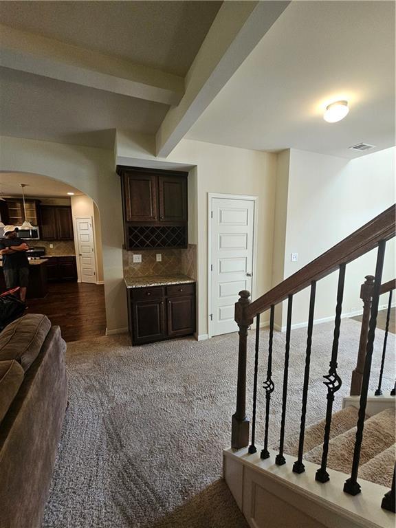 stairway featuring arched walkways, beam ceiling, and carpet floors