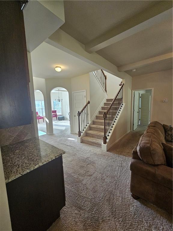 carpeted living room with arched walkways, stairway, baseboards, and beamed ceiling