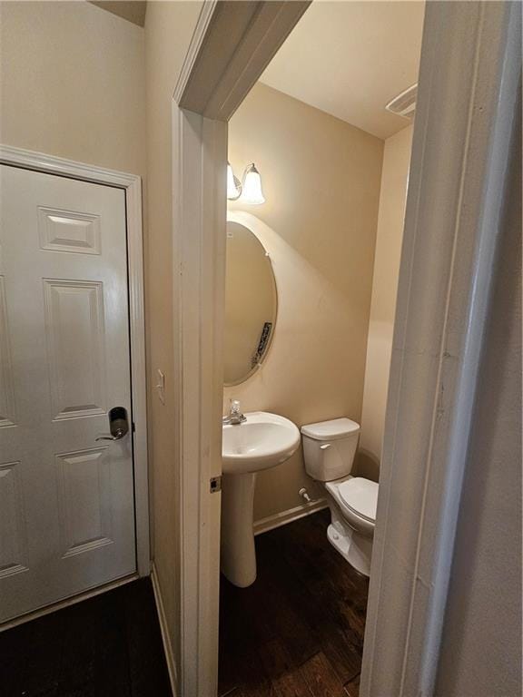 half bathroom featuring toilet, wood finished floors, baseboards, and a sink