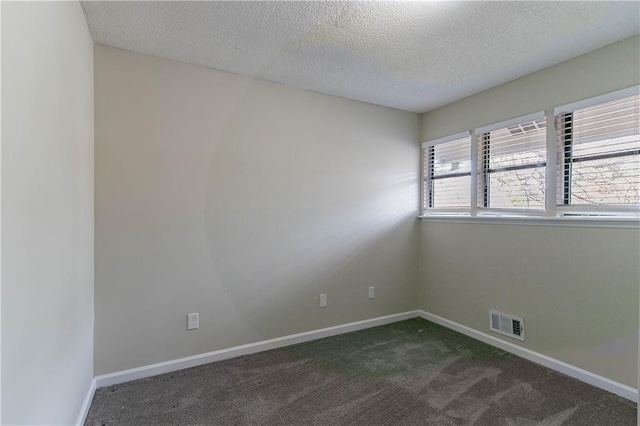 spare room featuring visible vents, dark carpet, a textured ceiling, and baseboards