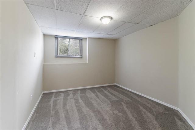 empty room with carpet flooring, a paneled ceiling, and baseboards