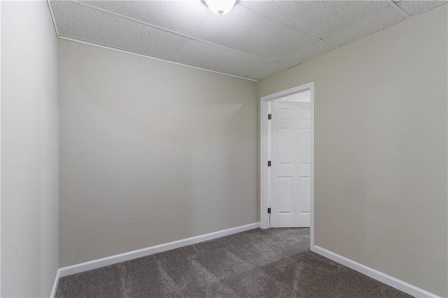 spare room featuring a paneled ceiling, dark carpet, and baseboards