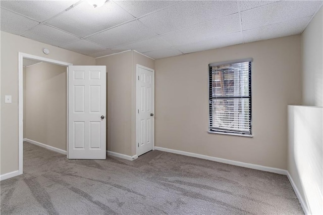 unfurnished room featuring baseboards, a drop ceiling, and light colored carpet