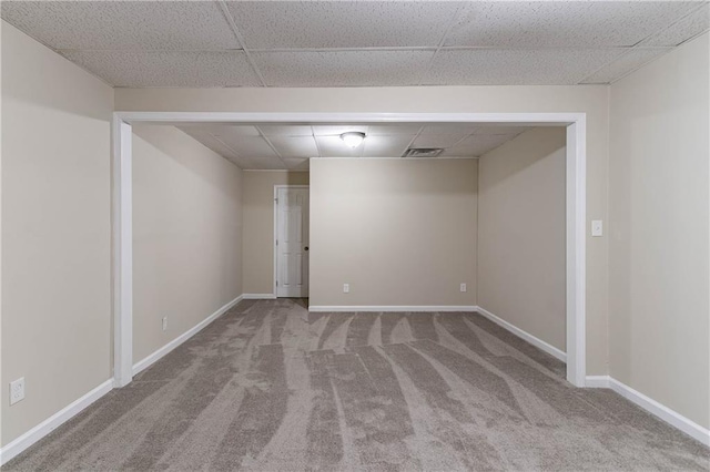 spare room featuring baseboards, visible vents, a drop ceiling, and light colored carpet