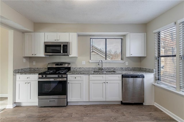 kitchen with appliances with stainless steel finishes, a healthy amount of sunlight, white cabinets, a sink, and light stone countertops