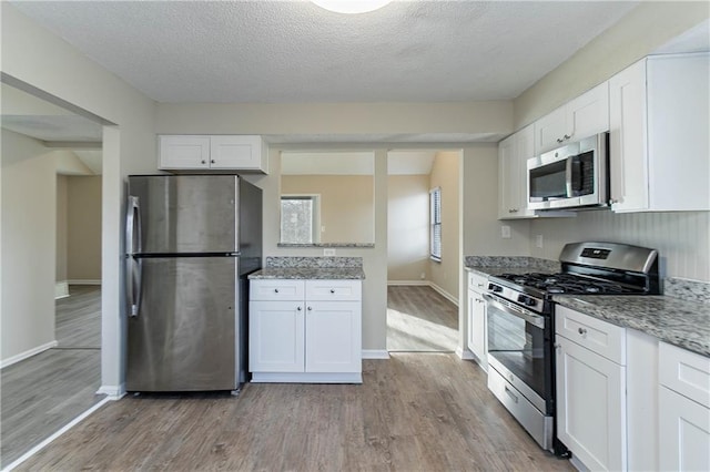 kitchen with appliances with stainless steel finishes, light wood-type flooring, white cabinets, and light stone counters