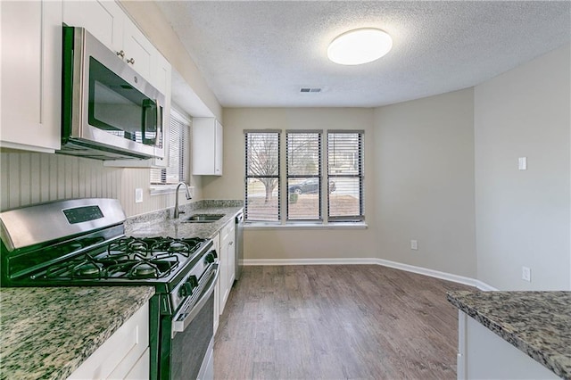 kitchen featuring stone counters, white cabinetry, stainless steel appliances, and a sink