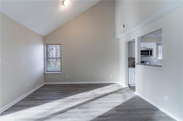 unfurnished living room with high vaulted ceiling, dark wood finished floors, visible vents, and baseboards