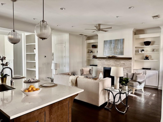 kitchen featuring dark wood-type flooring, hanging light fixtures, built in shelves, ceiling fan, and light stone countertops