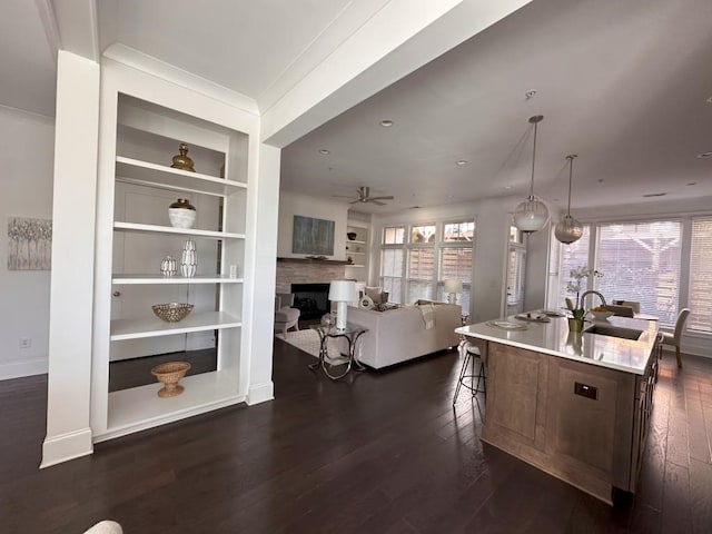 kitchen featuring ceiling fan, sink, hanging light fixtures, dark wood-type flooring, and a center island with sink