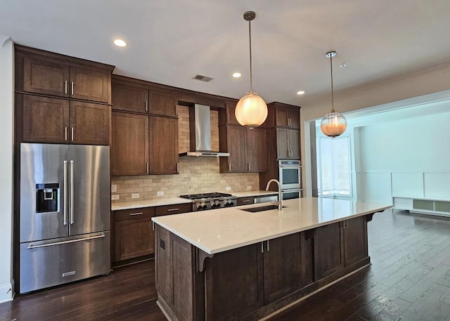 kitchen with sink, hanging light fixtures, wall chimney range hood, dark hardwood / wood-style flooring, and appliances with stainless steel finishes