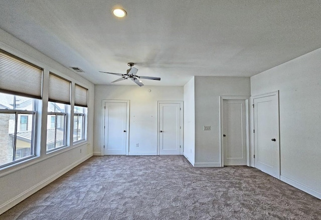 unfurnished bedroom with carpet flooring, ceiling fan, a textured ceiling, and two closets