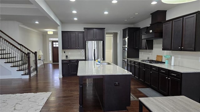 kitchen featuring appliances with stainless steel finishes, custom range hood, a sink, backsplash, and dark wood finished floors