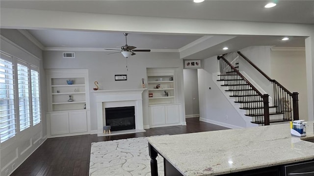 living area featuring ornamental molding, dark wood-style flooring, healthy amount of natural light, a ceiling fan, and stairs