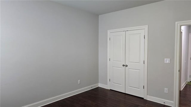 unfurnished bedroom featuring dark wood-style floors, baseboards, and a closet