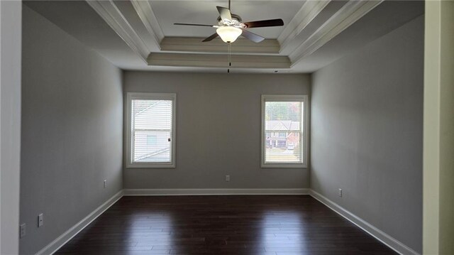 empty room with crown molding, a raised ceiling, dark wood-type flooring, a ceiling fan, and baseboards
