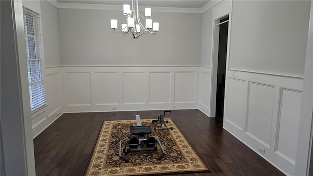 unfurnished dining area with a decorative wall, a chandelier, dark wood-style floors, crown molding, and wainscoting