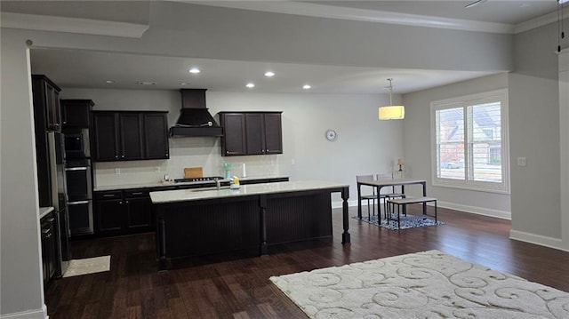 kitchen with custom exhaust hood, dark wood-type flooring, a center island with sink, baseboards, and tasteful backsplash