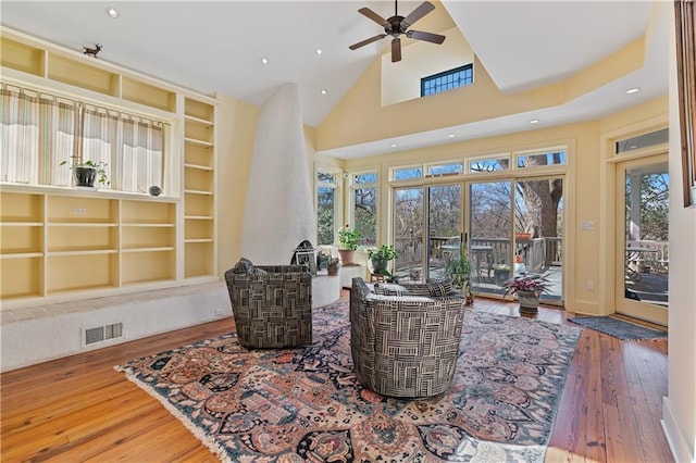 living area with visible vents, hardwood / wood-style flooring, ceiling fan, built in shelves, and high vaulted ceiling