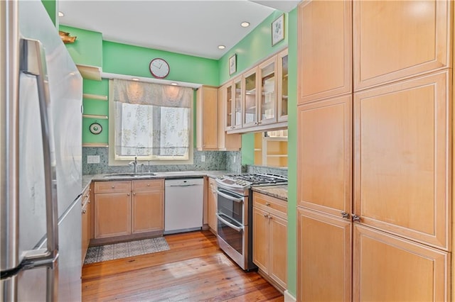 kitchen with tasteful backsplash, light wood-style flooring, appliances with stainless steel finishes, light stone countertops, and a sink