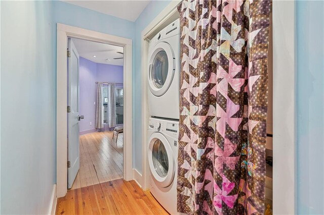 laundry area with stacked washer / drying machine, laundry area, light wood-style flooring, and baseboards