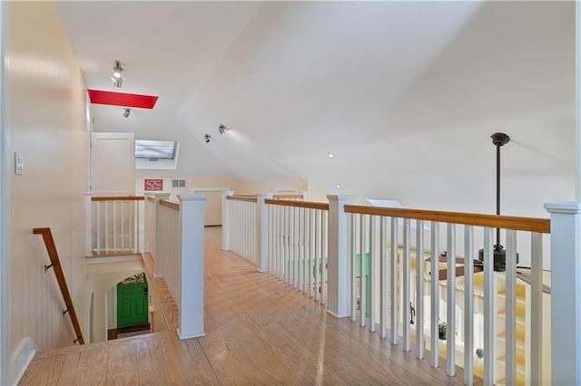 hallway with vaulted ceiling with skylight, visible vents, an upstairs landing, and wood finished floors