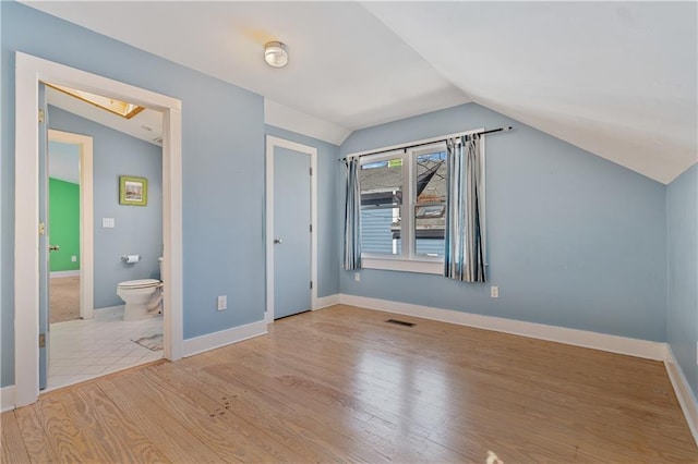 unfurnished bedroom with ensuite bathroom, wood finished floors, visible vents, baseboards, and vaulted ceiling