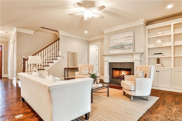 living area with crown molding, ceiling fan, dark wood finished floors, stairs, and a fireplace
