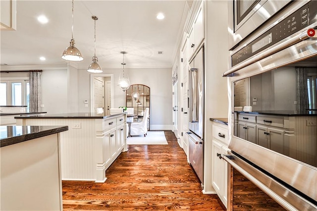 kitchen featuring dark countertops, crown molding, dark wood-style floors, stainless steel double oven, and white cabinetry
