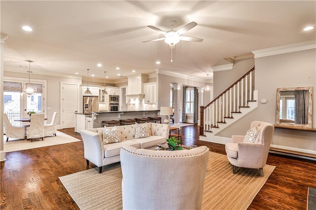 living room with dark wood-style floors, baseboards, stairs, crown molding, and ceiling fan with notable chandelier
