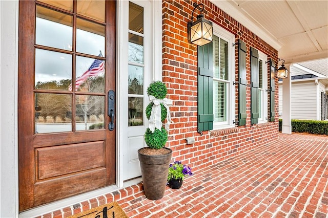 view of exterior entry featuring brick siding and covered porch