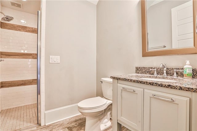 bathroom with visible vents, baseboards, toilet, a tile shower, and vanity