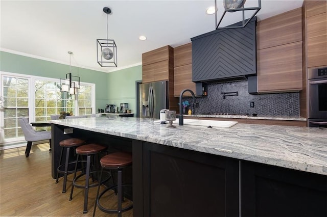 kitchen with a sink, backsplash, appliances with stainless steel finishes, ornamental molding, and hanging light fixtures
